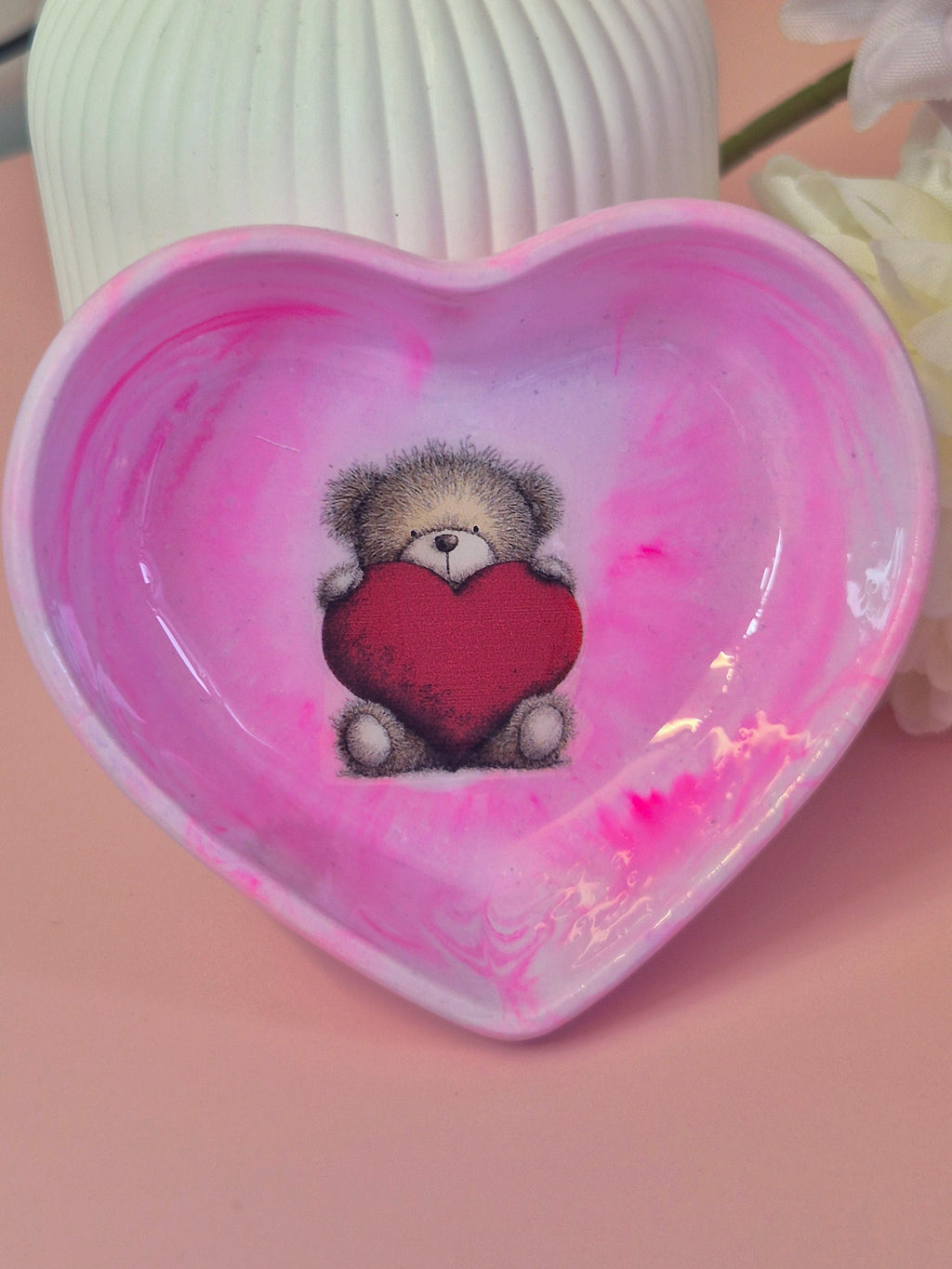 Heart-shaped trinket dish with a teddy bear holding a heart design on a pink background stood upright