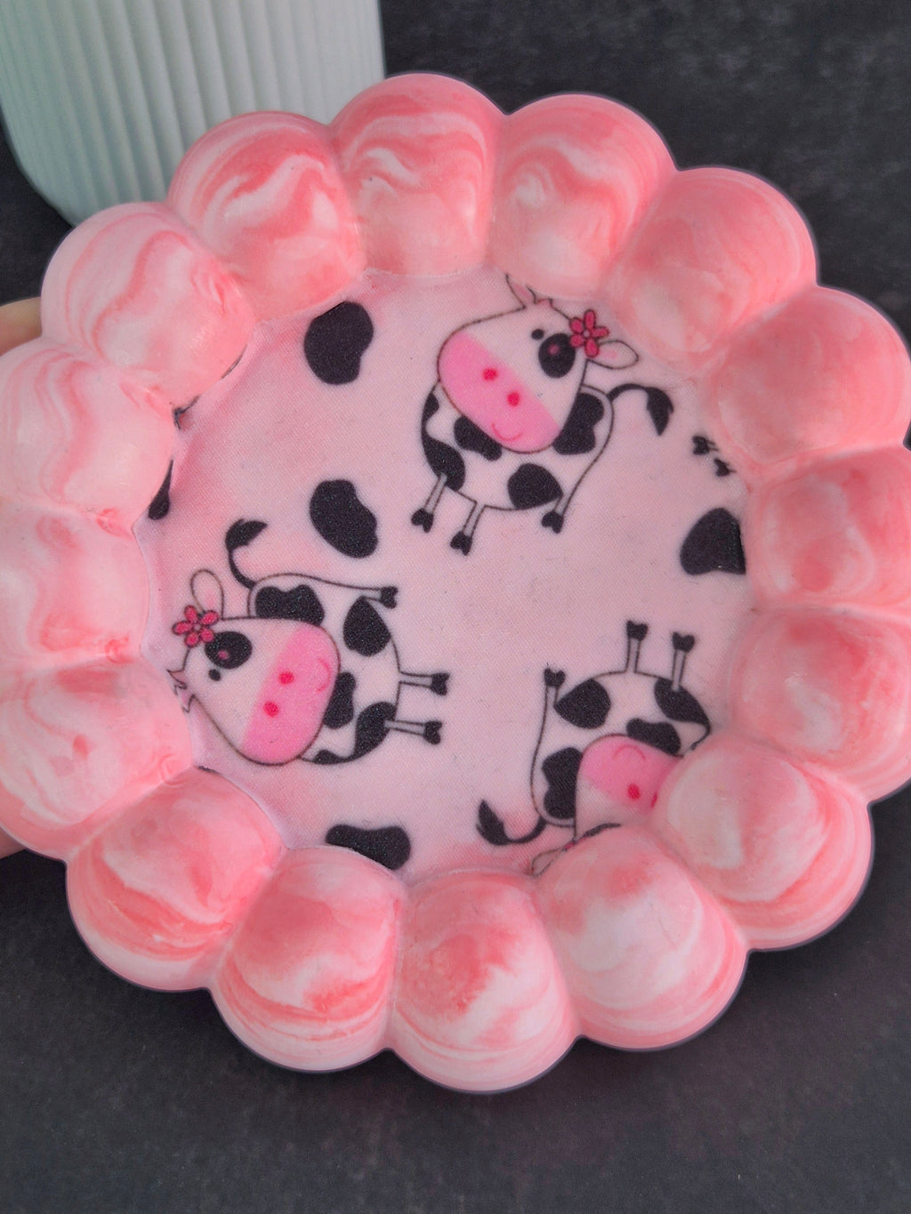 Top view of a handmade pink and white trinket tray featuring cartoon cow fabric decoupage and a raised bubble border.