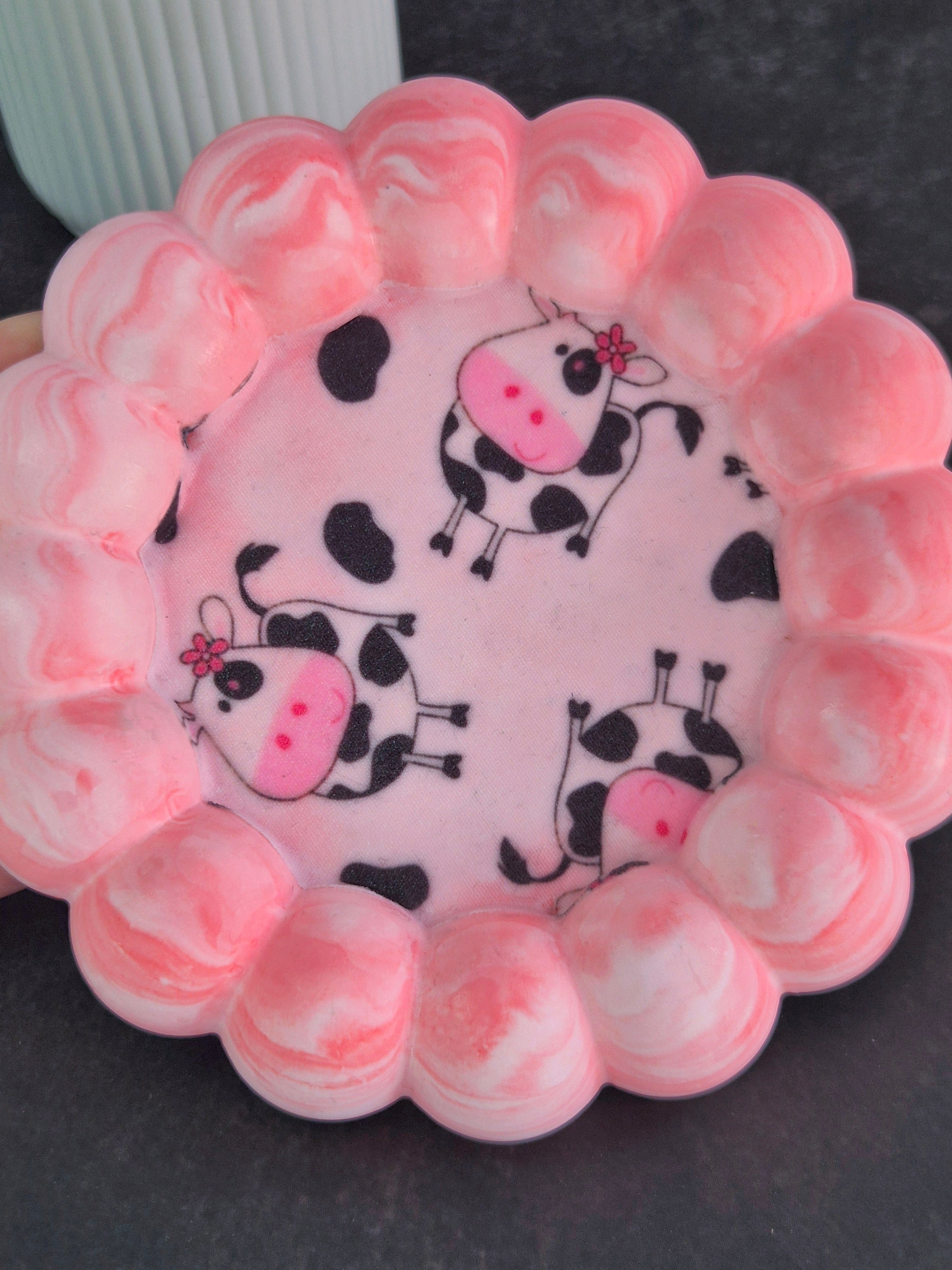 Top view of a handmade pink and white trinket tray featuring cartoon cow fabric decoupage and a raised bubble border.