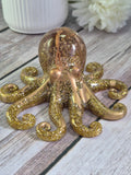 Gold glitter resin octopus ornament on a wooden surface with a white flower.