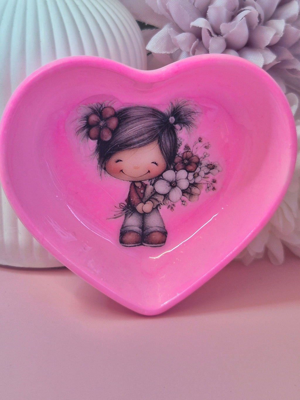 Heart-shaped pink trinket dish with a girl character holding flowers on a light pink background standing up
