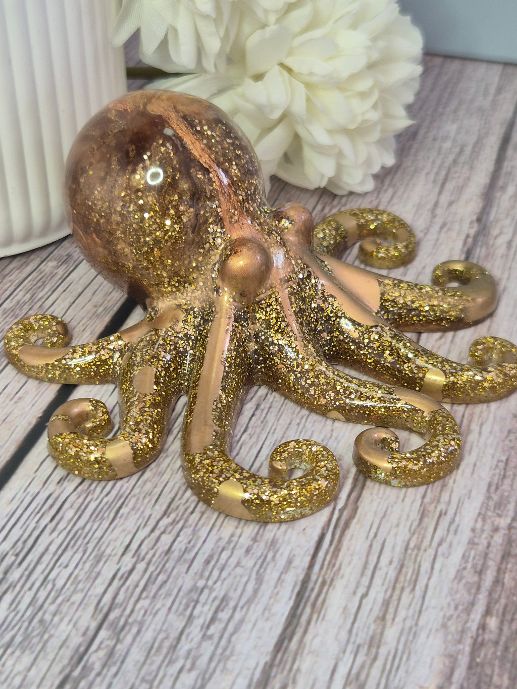 Decorative gold resin octopus on a wooden surface with white flowers.
