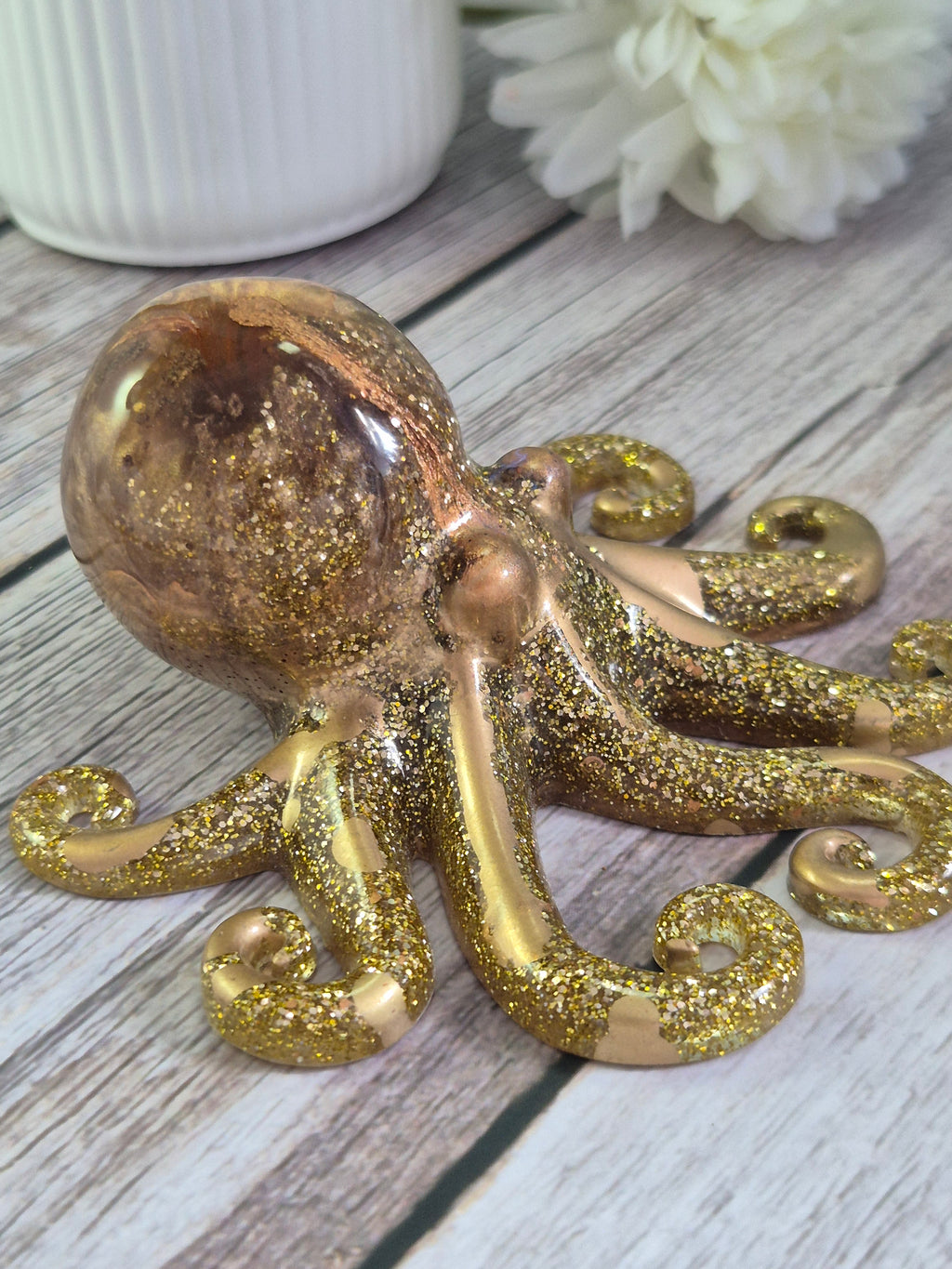 Gold glittery resin octopus ornament on a wooden surface with a white flower.