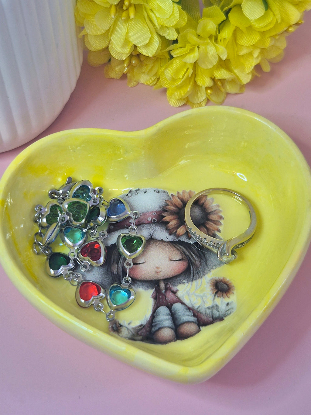 Heart-shaped yellow trinket dish with jewelry and a decorative figure on a pink background