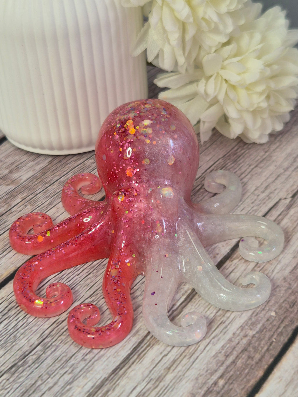 Pink resin glittery octopus octopus on a wooden surface with a white flower in the background