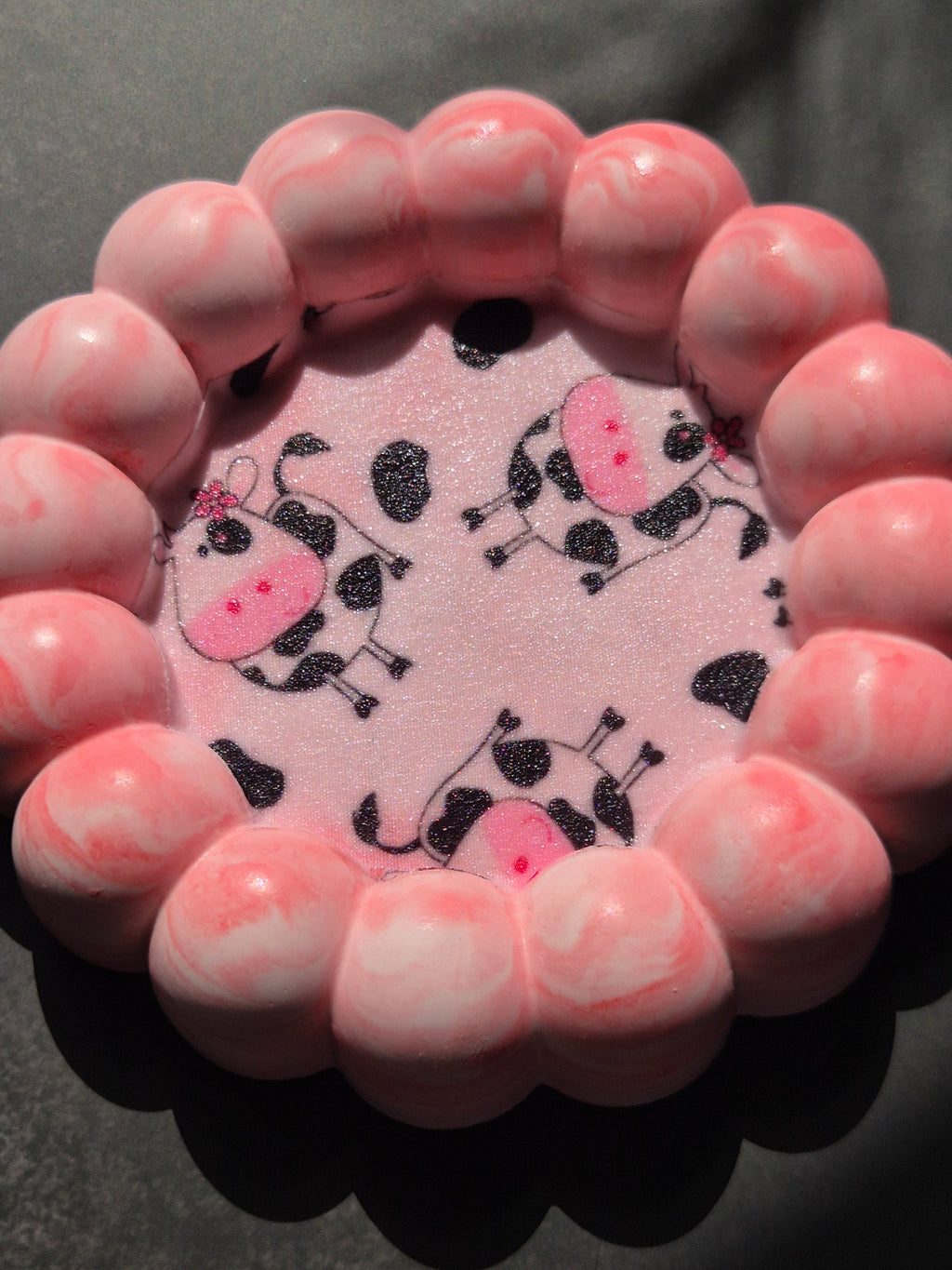 Sunlit close-up of the cow-print decoupage centre, showing the sealed fabric surface and pink marbled bubble edge.