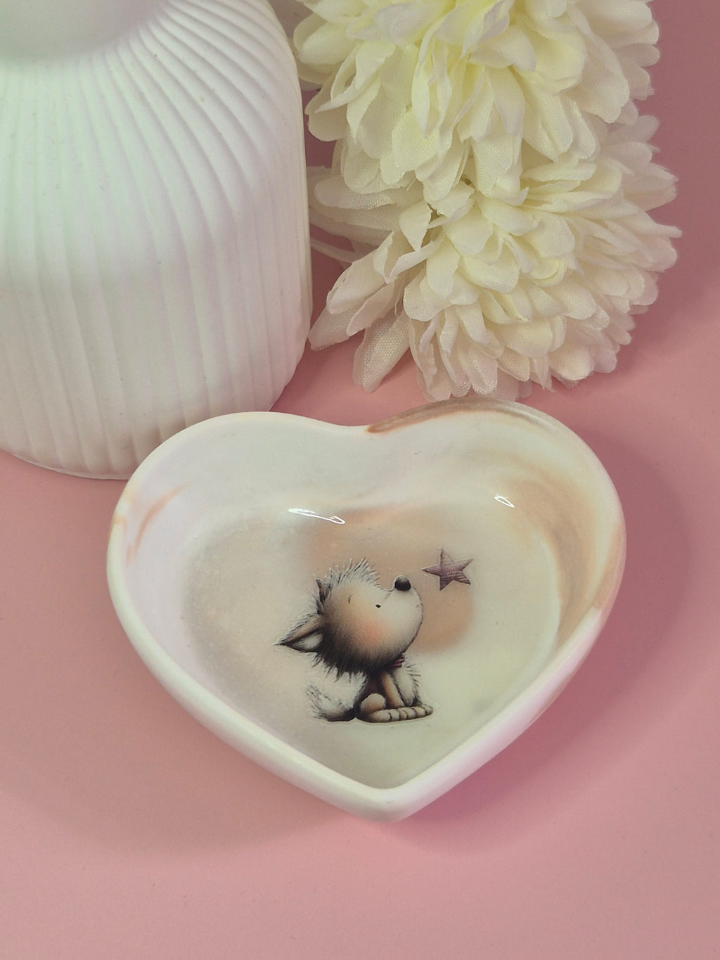 Heart-shaped Puppy Wishes Trinket Dish displayed on a pink surface with soft floral styling in the background.