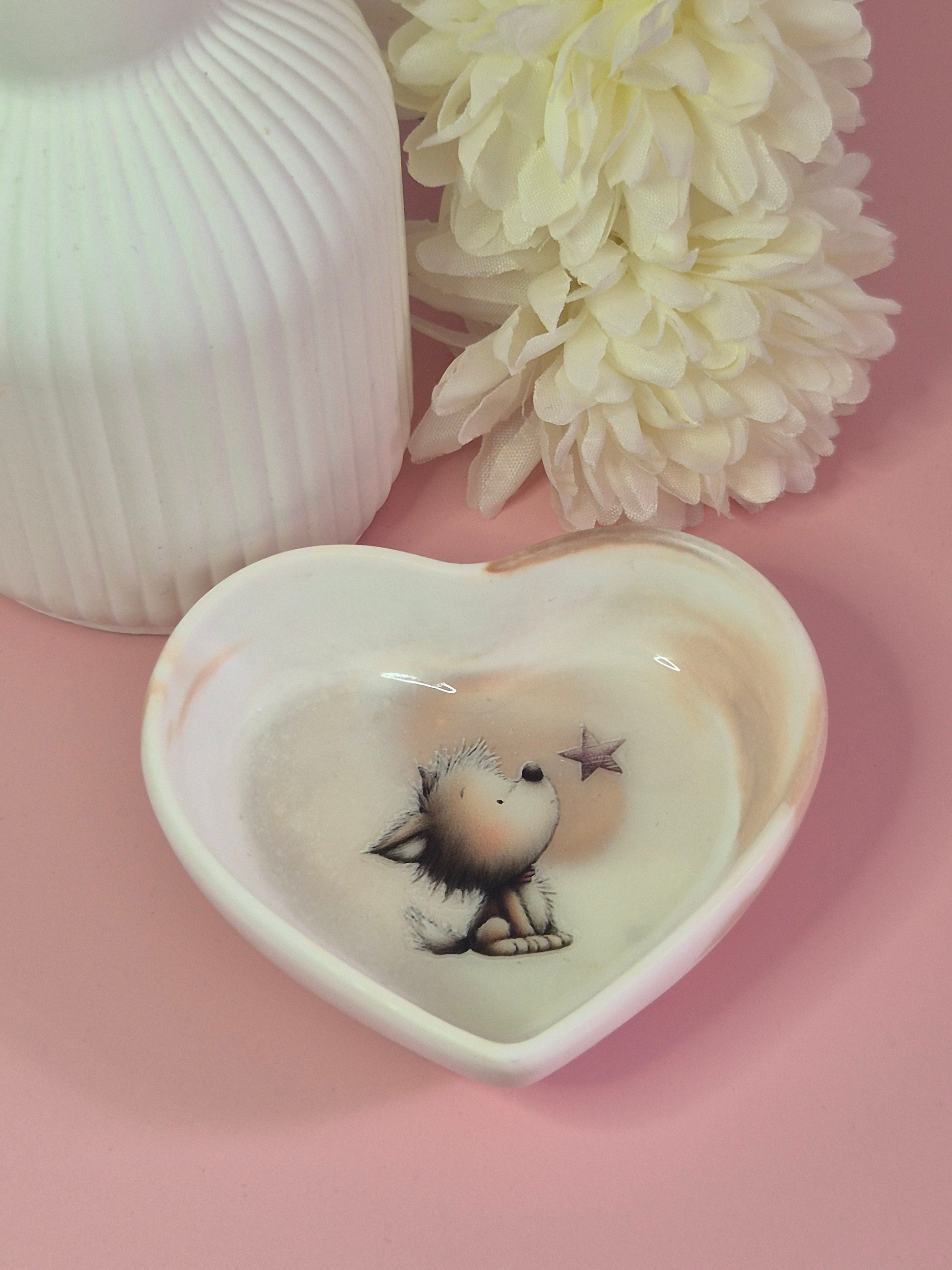Heart-shaped Puppy Wishes Trinket Dish displayed on a pink surface with soft floral styling in the background.