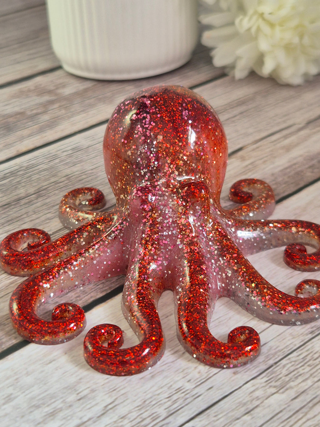 Red pink handmade resin octopus on a wooden surface with flowers in the background