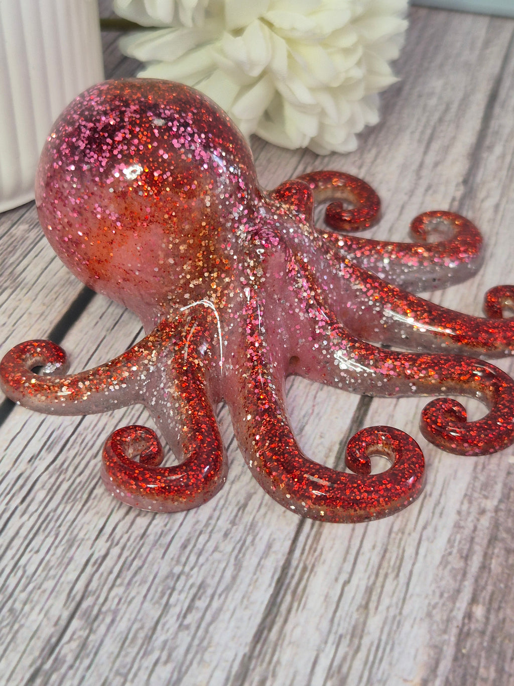 Decorative pink and red glittery octopus on a wooden surface with a white flower.