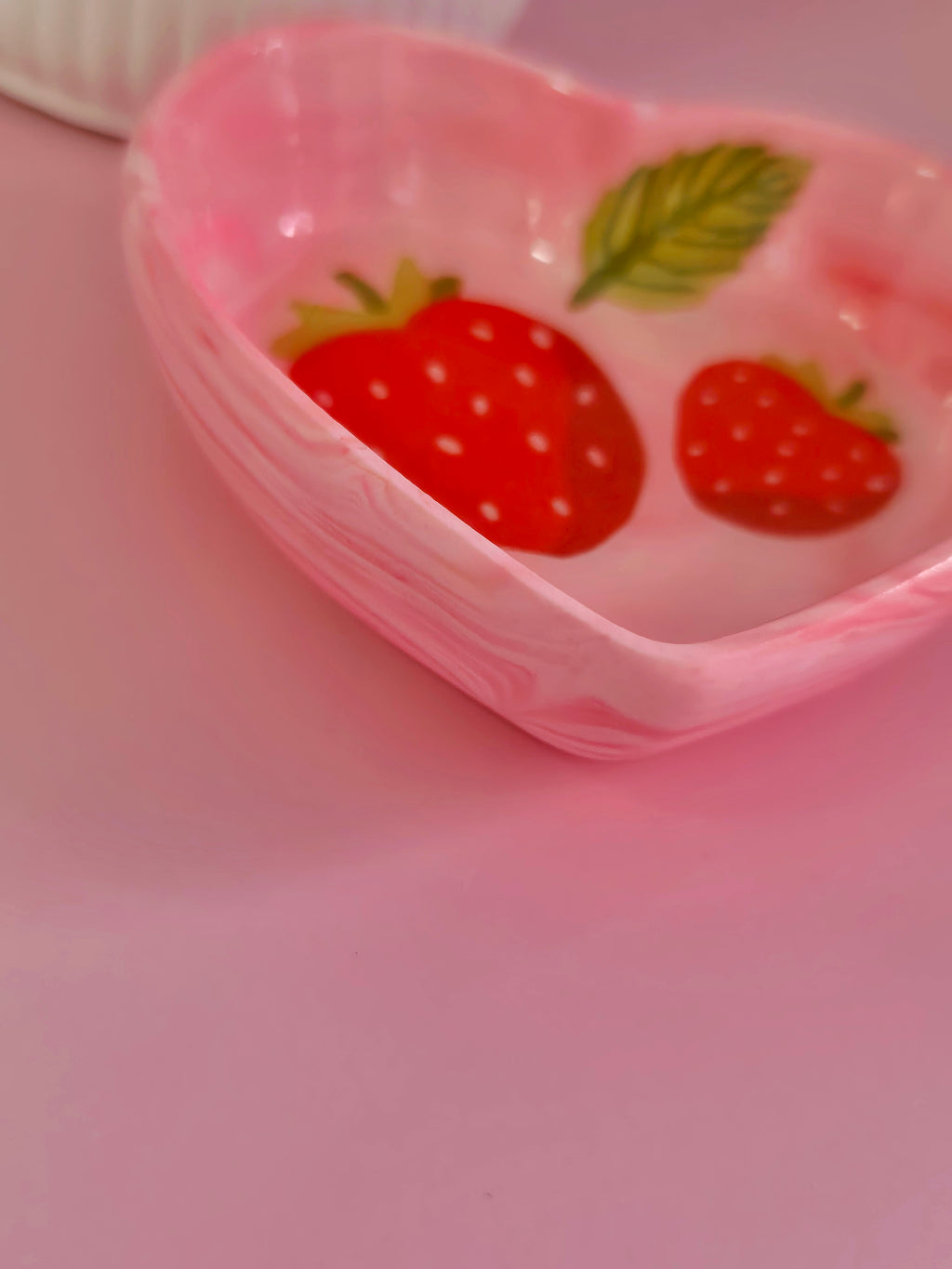 Close-up side view of a pink strawberry heart trinket dish showing the raised heart edge, glossy finish and red strawberry details inside.