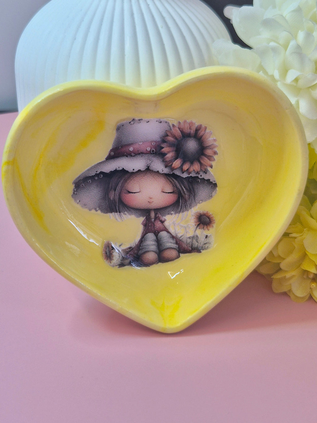 Heart-shaped yellow dish with a girl and sunflowers stood up on a pink surface