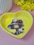 Heart-shaped yellow trinket dish with a cute girl and sunflowers on a pink background.