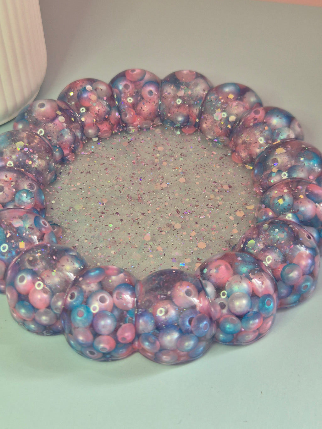 Handmade circular resin trinket tray with a raised bubble border with teal, pink beads and a glitter centre
