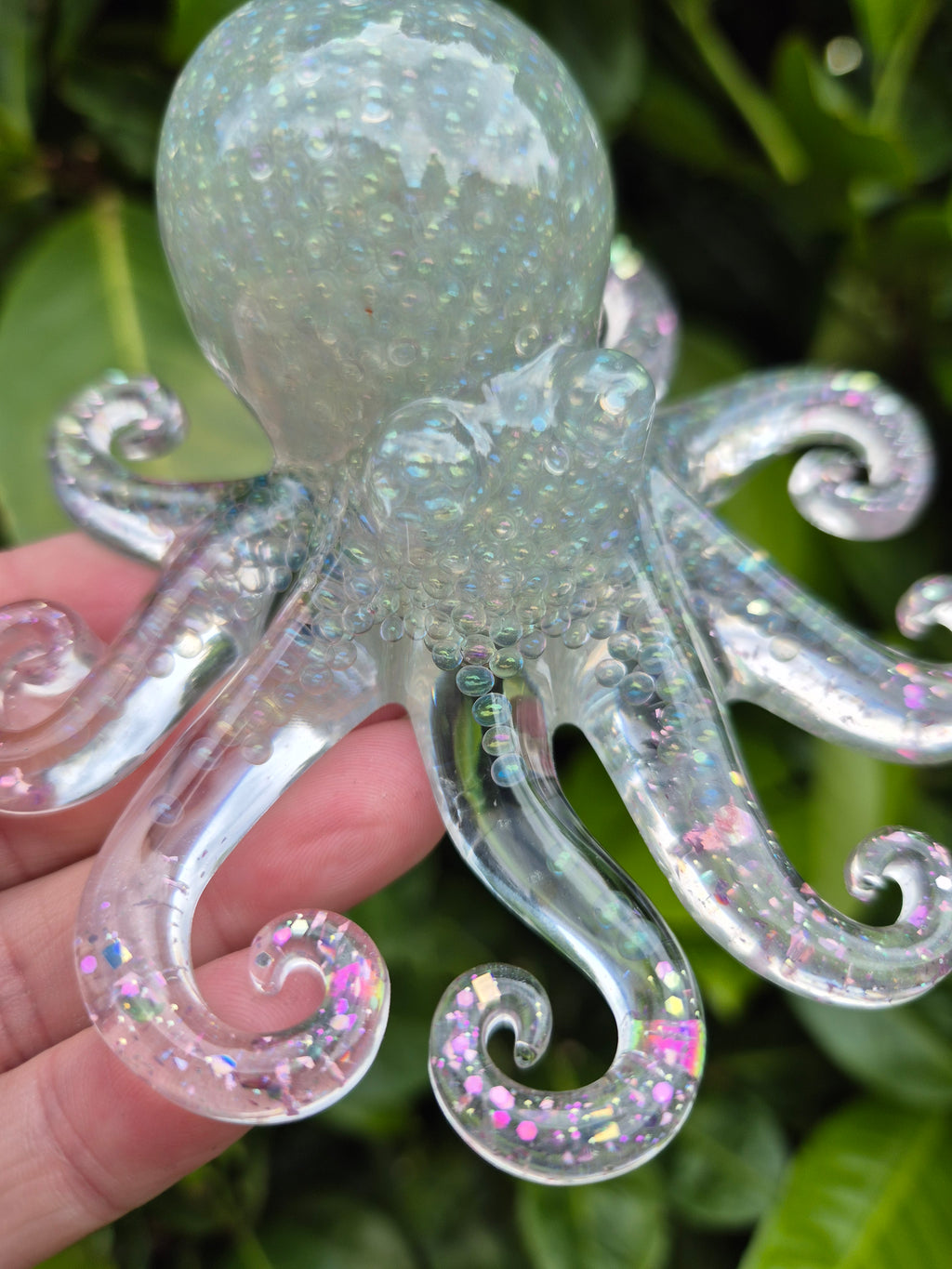 Resin octopus with tiny beads, held by a hand against a blurred green background