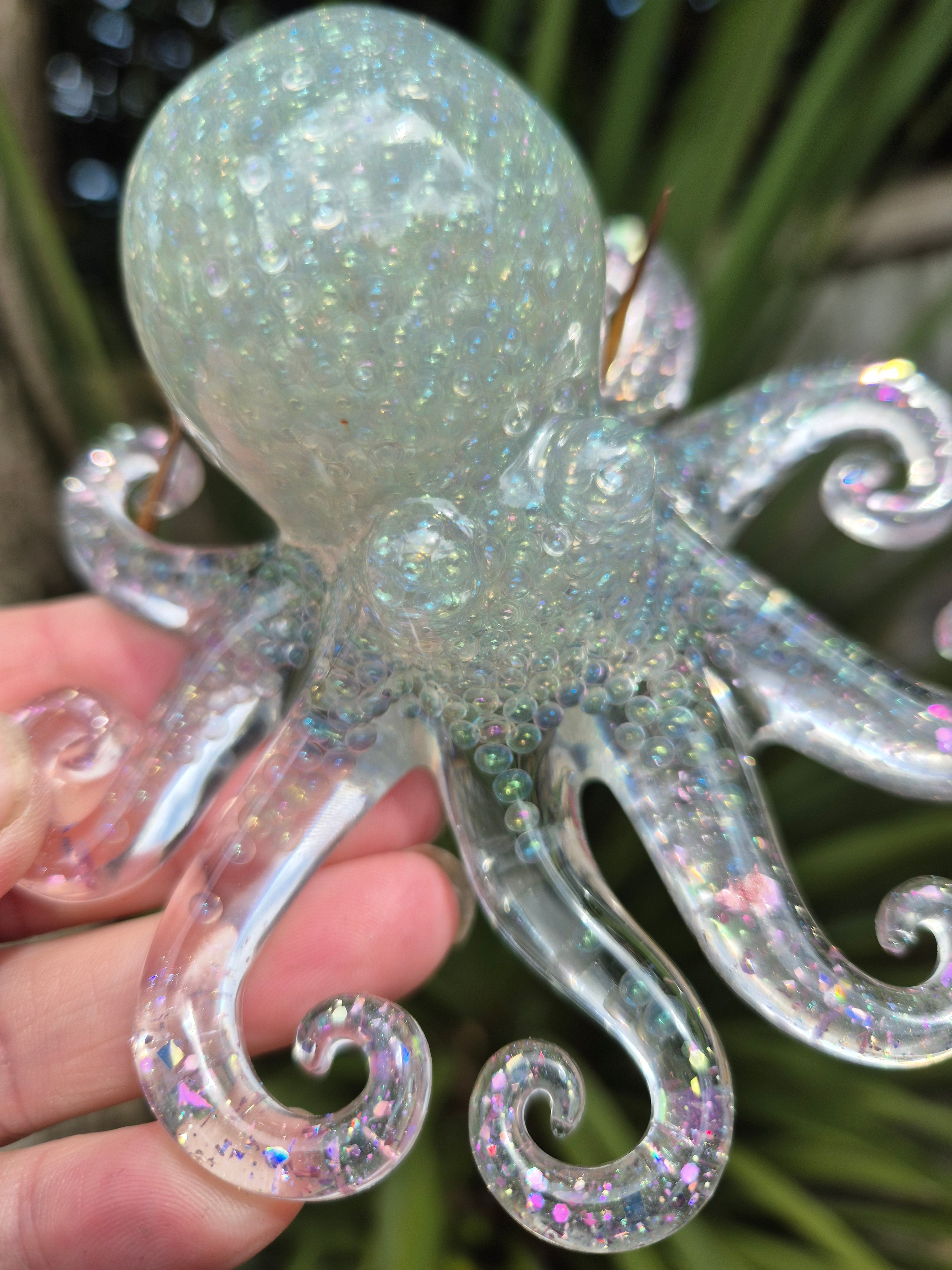 Resin octopus with tiny beads, held by a hand against a blurred green background