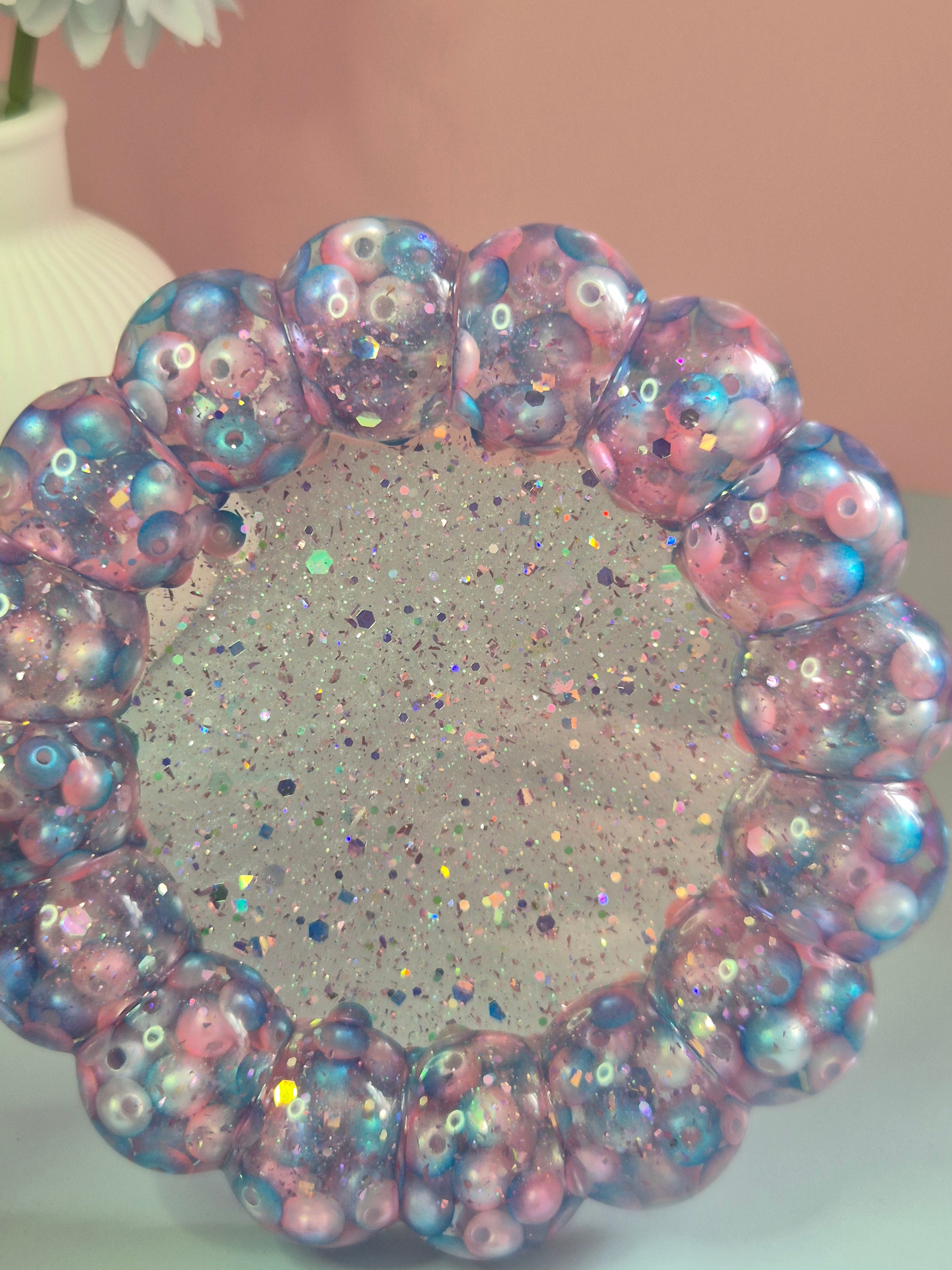 Handmade circular resin trinket tray with a raised bubble border with teal, pink beads and a glitter centre, close up
