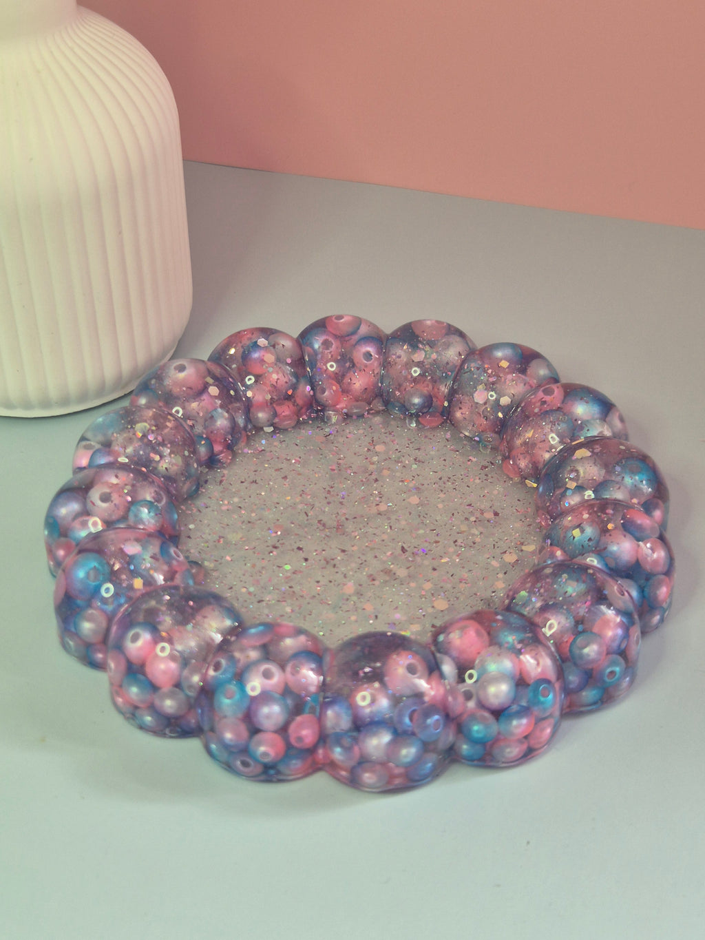 Handmade circular resin trinket tray with a raised bubble border with teal, pink beads and a glitter centre